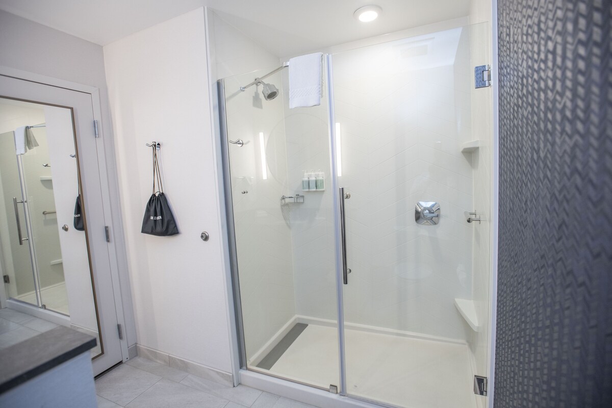 Un baño moderno con cabina de ducha de vidrio, un lavamanos blanco y un espejo.