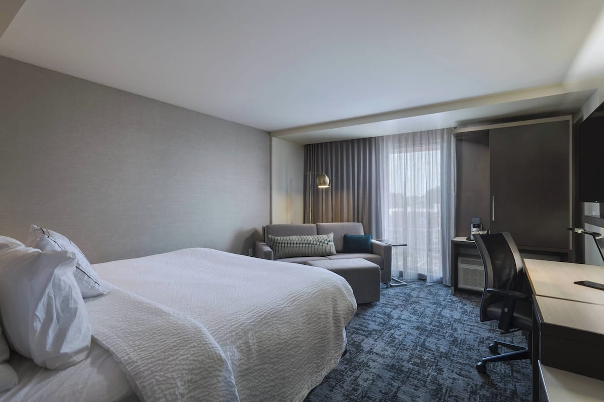 A hotel room with a large bed, a desk, a chair, and a sofa.