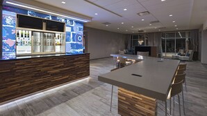 A modern hotel lobby with a bar area, a large dining table, and a seating area with chairs.