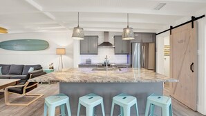 Una cocina moderna con isla de mármol, taburetes de bar e iluminación colgante.
