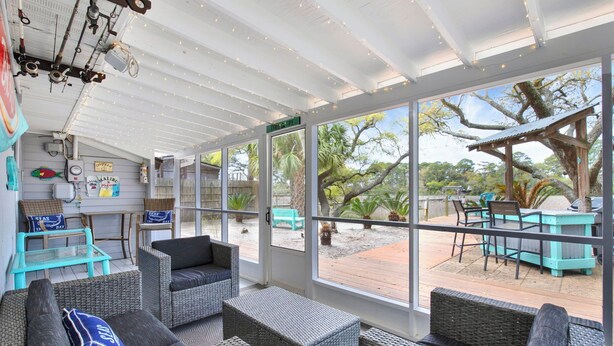 Un espacio de estar al aire libre cubierto con mobiliario de mimbre, ventanas amplias y vistas al exterior.