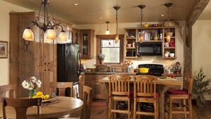 Una cocina con armarios de madera, un refrigerador negro, una mesa de comedor con sillas y lámparas colgantes.