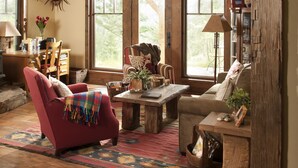 Un salón espacioso con techo alto, vigas de madera, chimenea y ventanas grandes.