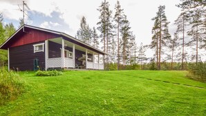A two-story house with a red exterior and a porch. It is surrounded by a well-maintained lawn and tall pine trees. - Sieralahden lomakylä, mökki 2 by Interhome (Savonlinna)
