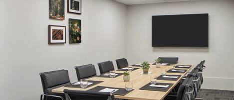 Una sala de conferencias con una larga mesa, sillas negras, cuadros en la pared y una pantalla para proyector.