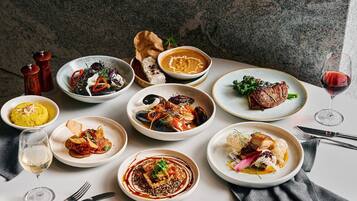 A variety of dishes on a table, including seafood, meat, and vegetables, with a wine glass and cutlery.