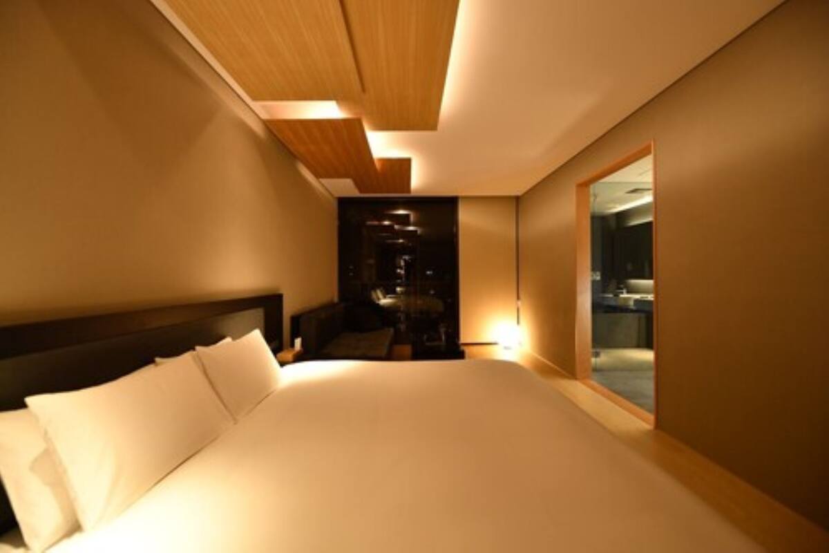 A modern hotel room with a large bed, a wooden ceiling, and a view of the city through a large window.