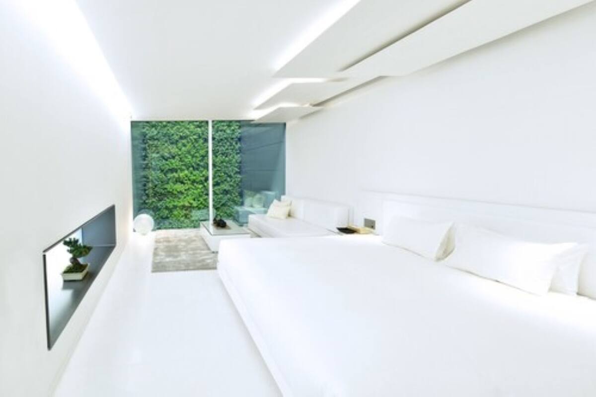 A modern bedroom with a large bed, a bedside table, and a view of greenery through a glass door.