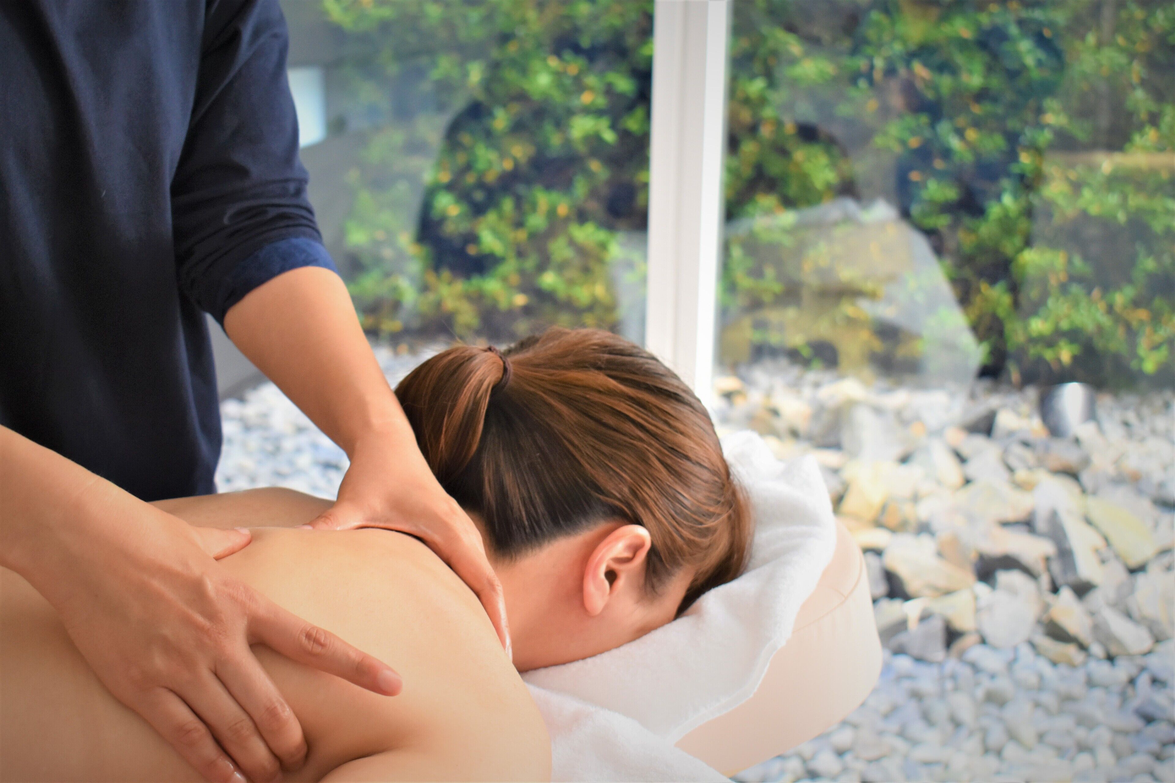 Eine Massageanwendung in einem Spa-Ambiente mit Blick auf Felsen und Grünpflanzen.
