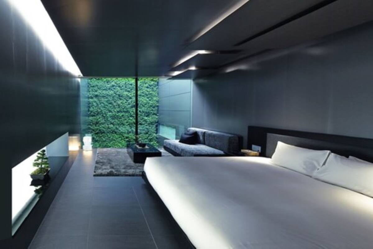 A modern bedroom with a large bed, a small seating area, and a view of greenery through a window.