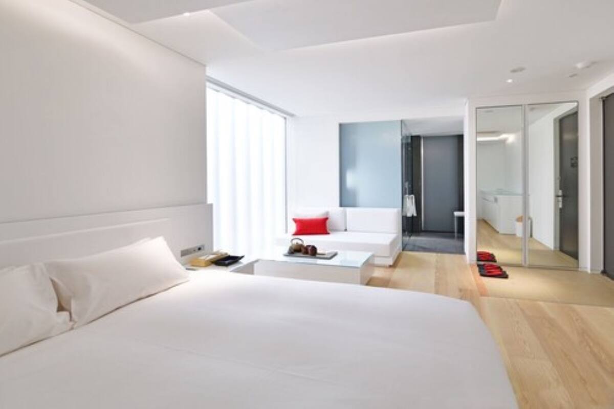 A modern hotel room with a large bed, a small seating area, and a view of the hallway.