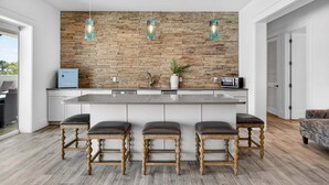 Une cuisine moderne dotée d’un îlot central, de tabourets de bar, de luminaires suspendus et d’un pare-feu en pierre.