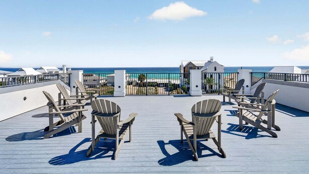 Une terrasse sur le toit, dotée de chaises Adirondack, offrant une vue sur l’océan et donnant sur un bâtiment à la façade blanche.