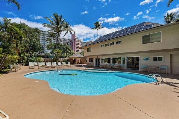 A swimming pool with lounge chairs, a covered seating area, and a building with solar panels.