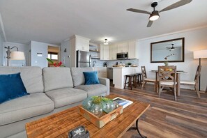Een moderne woonkamer met een grijze bank, een houten salontafel en een eethoek met een houten tafel en stoelen.