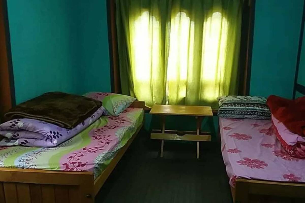 A small room with two single beds, a wooden bench, and a window with green curtains.