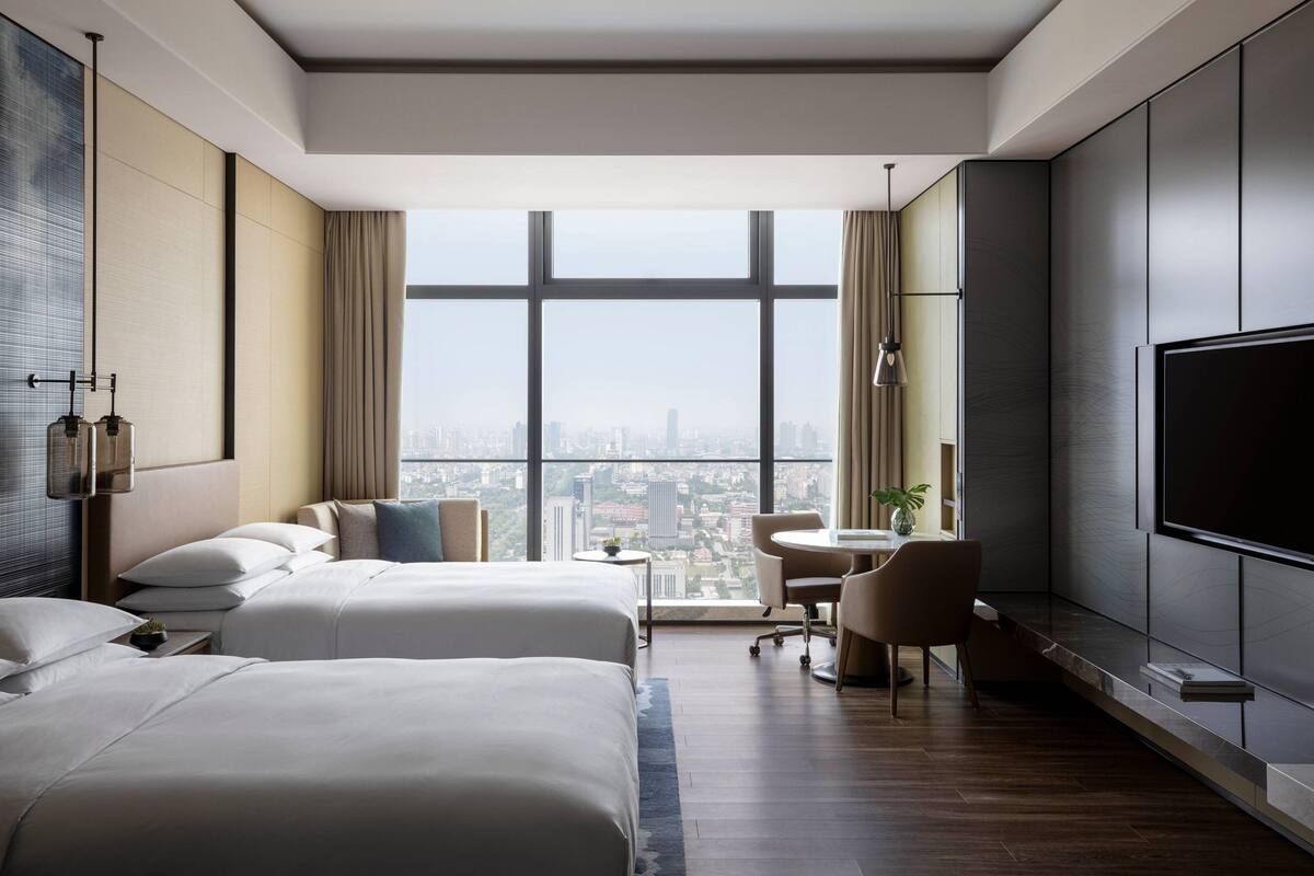 Una habitación de hotel moderna con dos camas, un escritorio, una silla y un televisor grande.