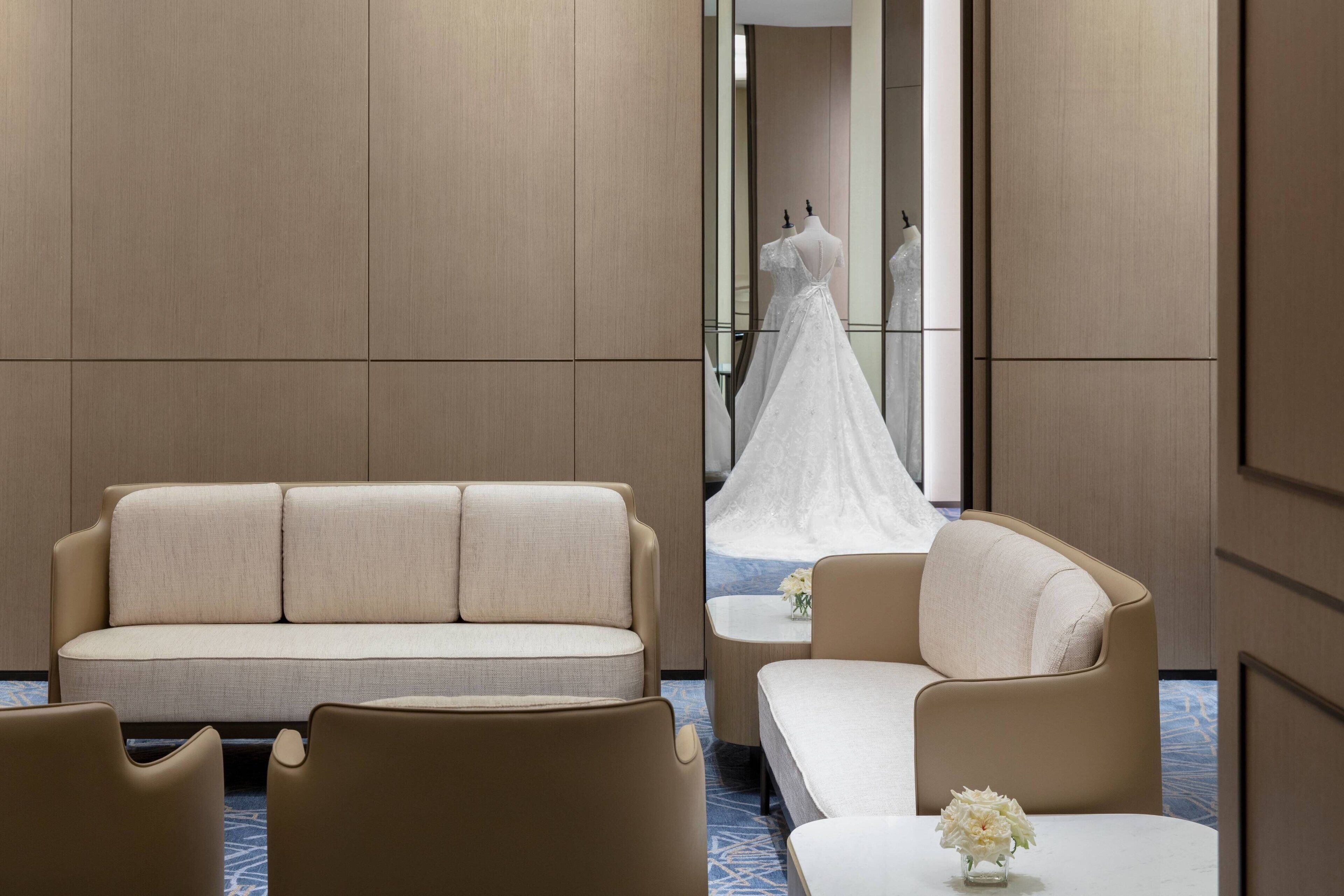 A hotel room with a sofa, armchair, and a small table with a vase of flowers.
