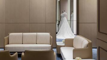 A hotel room with a sofa, armchair, and a small table with a vase of flowers.