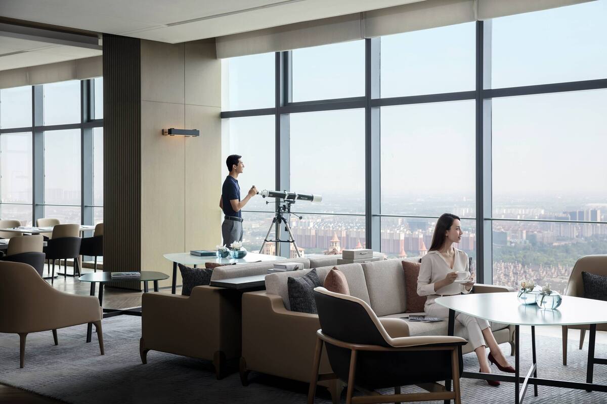 Una habitación de hotel moderna con ventanas amplias, un telescopio y zonas de estar confortables.