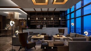 A modern lounge area with a large bookshelf, comfortable seating, and a city view through large windows. - Zhangjiagang Marriott Hotel (Suzhou)