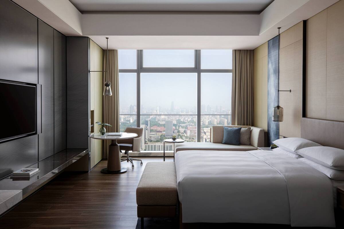 Una habitación de hotel moderna con una cama grande, un escritorio, una silla, un televisor y vistas a la ciudad.