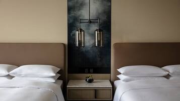A hotel room with two beds, a nightstand with a plant, and a wall-mounted light fixture.