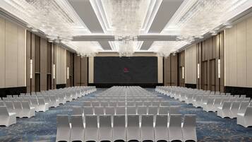 Un salón de conferencias con hileras de sillas blancas, una pantalla grande al frente y un techo con candelabro.