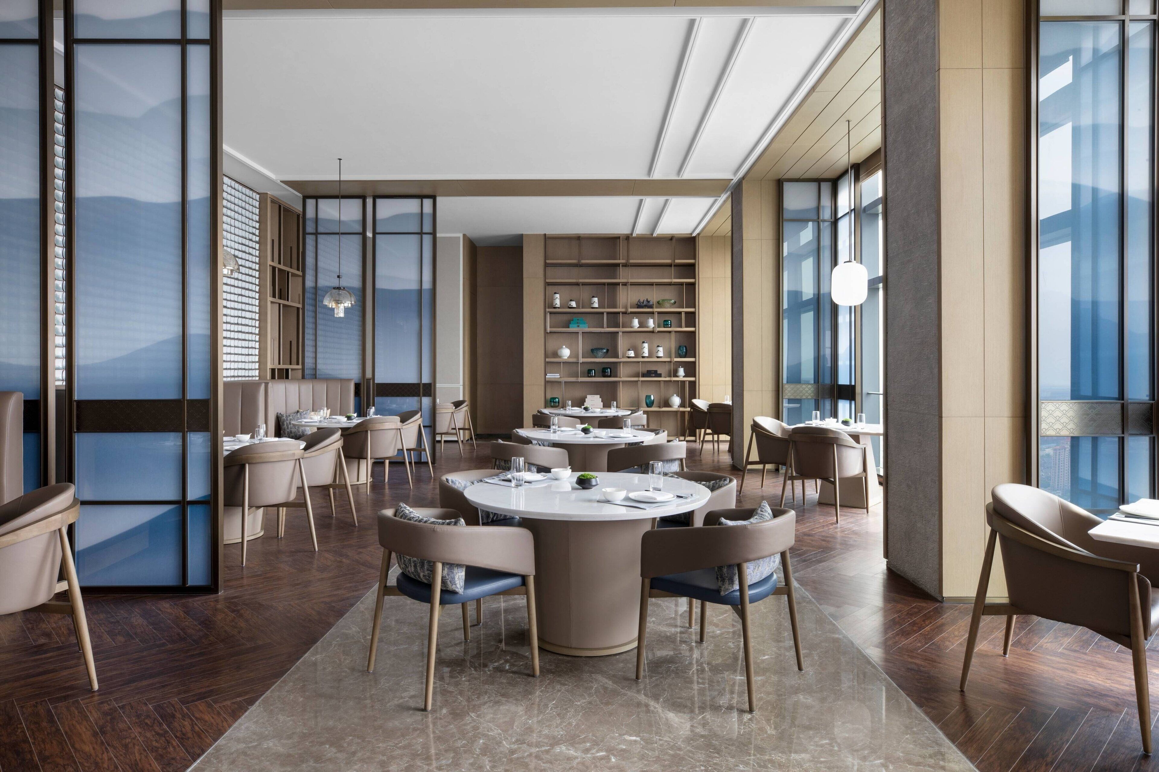 Un espace repas moderne avec des tables et des chaises rondes, une grande bibliothèque et de grandes fenêtres.