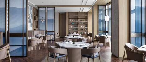 Un área de comedor moderna con mesas y sillas redondas, una amplia estantería y grandes ventanales.