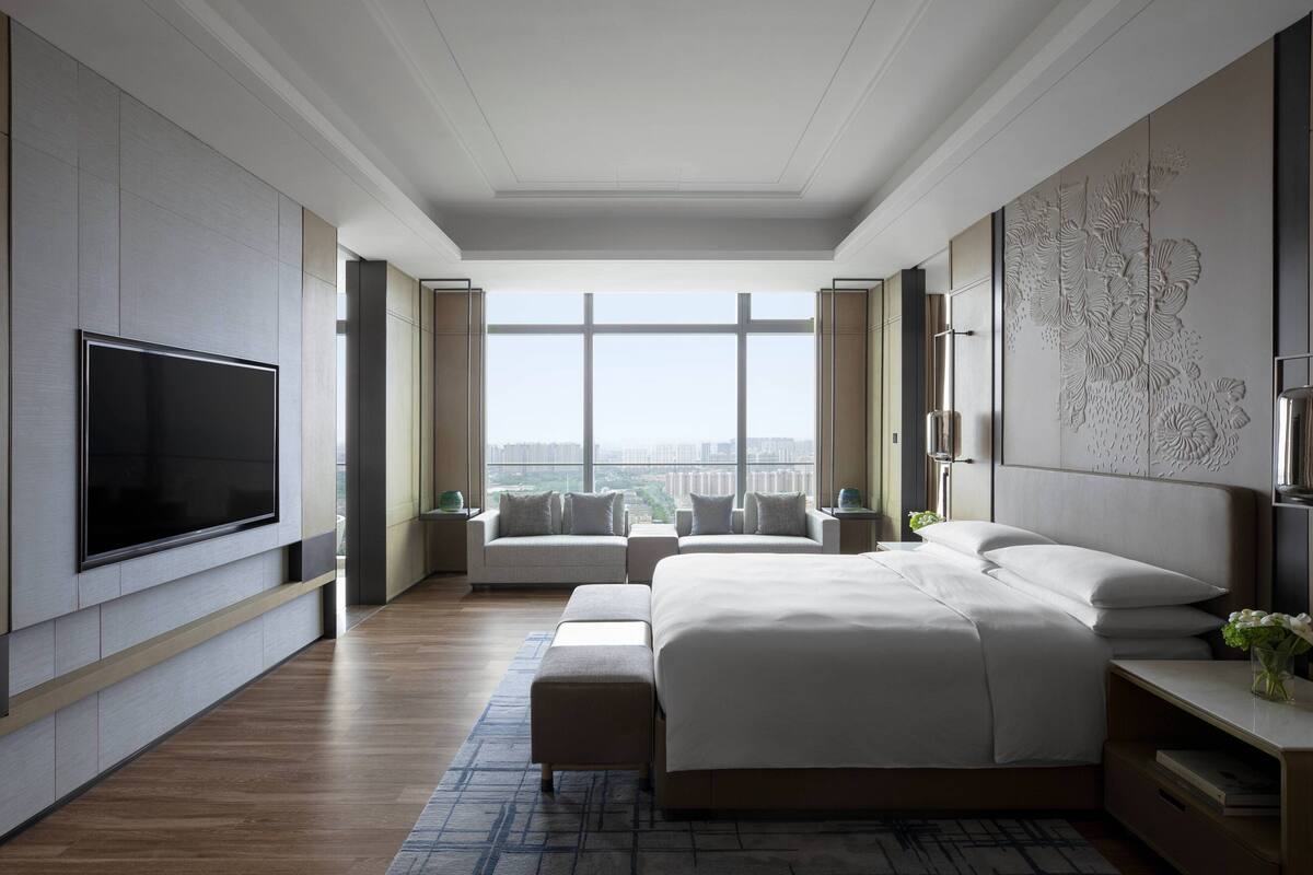 Un dormitorio moderno de hotel con una cama grande, televisión de pantalla plana y vista a la ciudad.