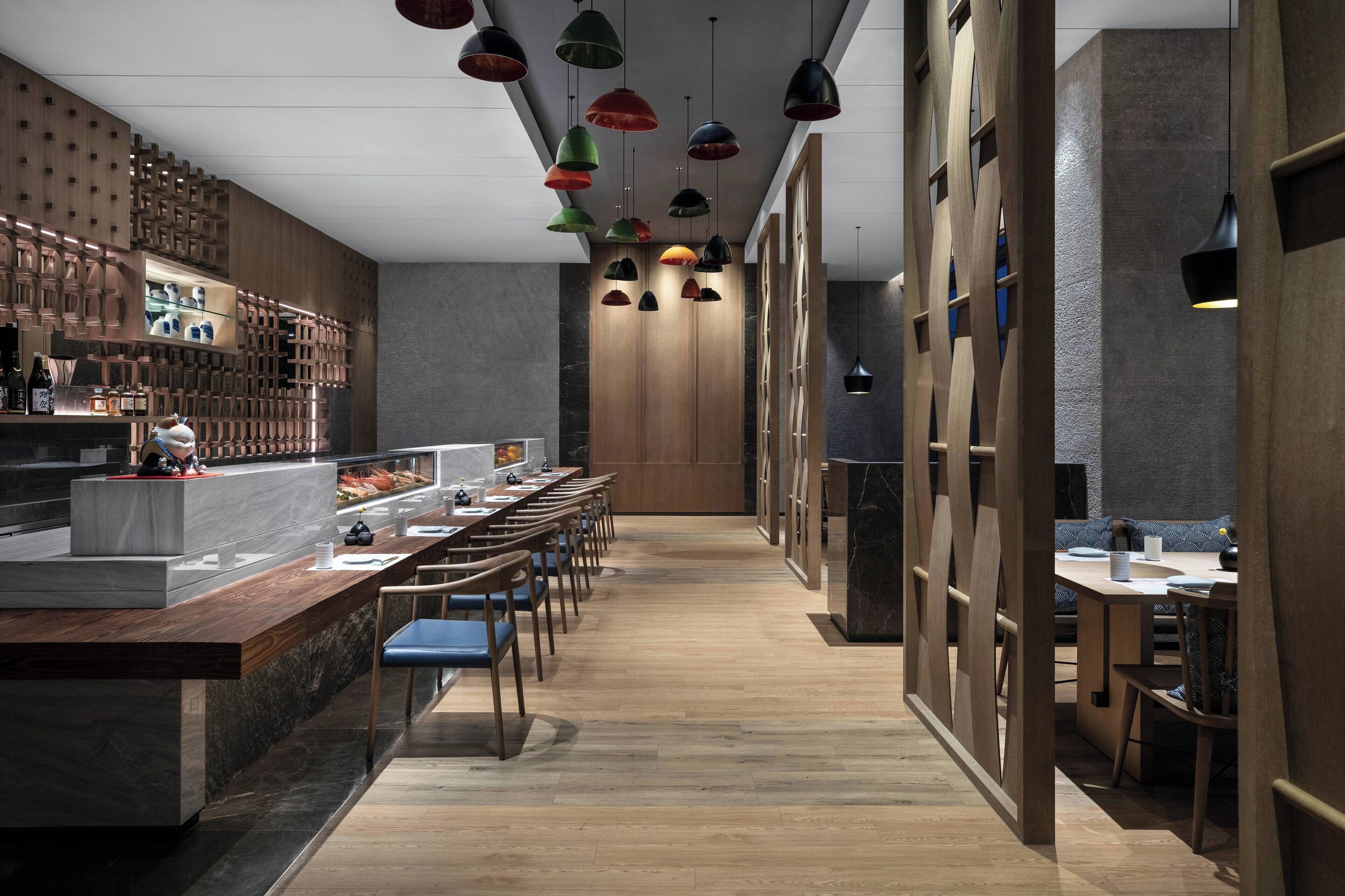 A modern restaurant with a long counter, wooden paneling, and colorful pendant lights.
