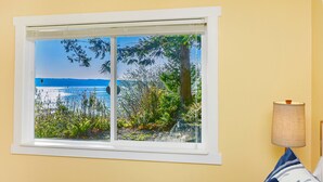 Ein Zimmer mit Fensterblick auf eine natürliche Landschaft, einem Bett mit blau-weißer Bettwäsche und einer Lampe auf der rechten Seite.
