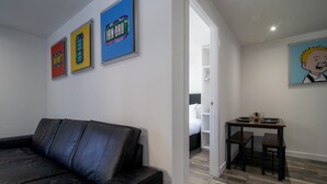 Una sala moderna con un sofá de cuero negro, una mesa de comedor con dos sillas y una pequeña área de cocina.