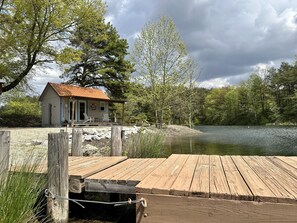 A rustic cabin with a metal roof, a dock extending into a lake, surrounded by trees and a stone wall. - No Wake Zone (Jasonville)