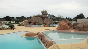 Un área de piscina con varias piscinas, formaciones rocosas y un tobogán.