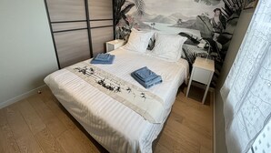Un dormitorio con cama, mesitas de noche, un mural en la pared y una cortina.