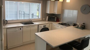 A modern kitchen with white cabinetry, a built-in dishwasher, a gas stove, and pendant lighting.