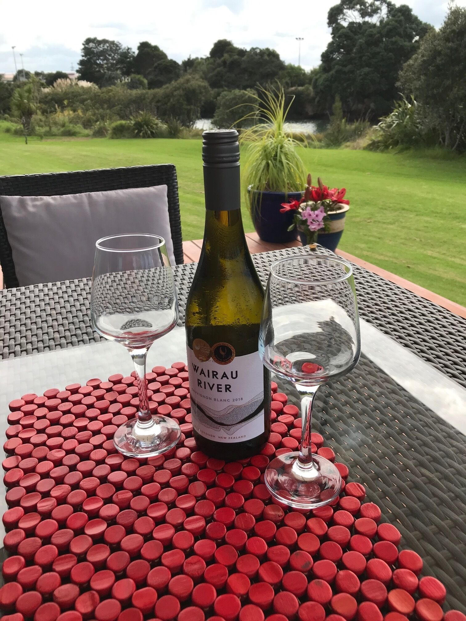A bottle of Wairau River Sauvignon Blanc 2018 wine on a table with two glasses and red wine bottle caps.