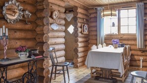 A log cabin interior with a dining table, chairs, a wooden ceiling, and a window with curtains. - Nice home in Högsby with kitchen (Högsby)