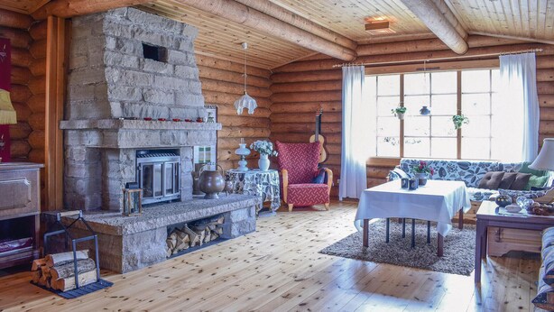 A cozy log cabin interior with a stone fireplace, wooden furniture, and a large window with curtains. - Nice home in Högsby with kitchen (Högsby)