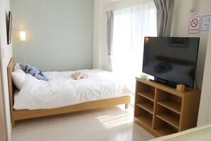 A bedroom with a bed, a TV on a wooden stand, and a window with curtains.