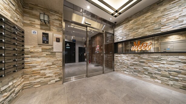 Um lobby moderno com paredes de pedra, um elevador de vidro e uma placa com a palavra 'Meet'.
