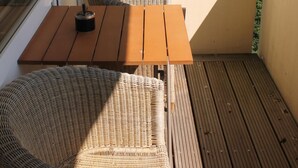 Varanda com mobiliário de vime e mesa de madeira, com vista para uma área residencial e o mar.