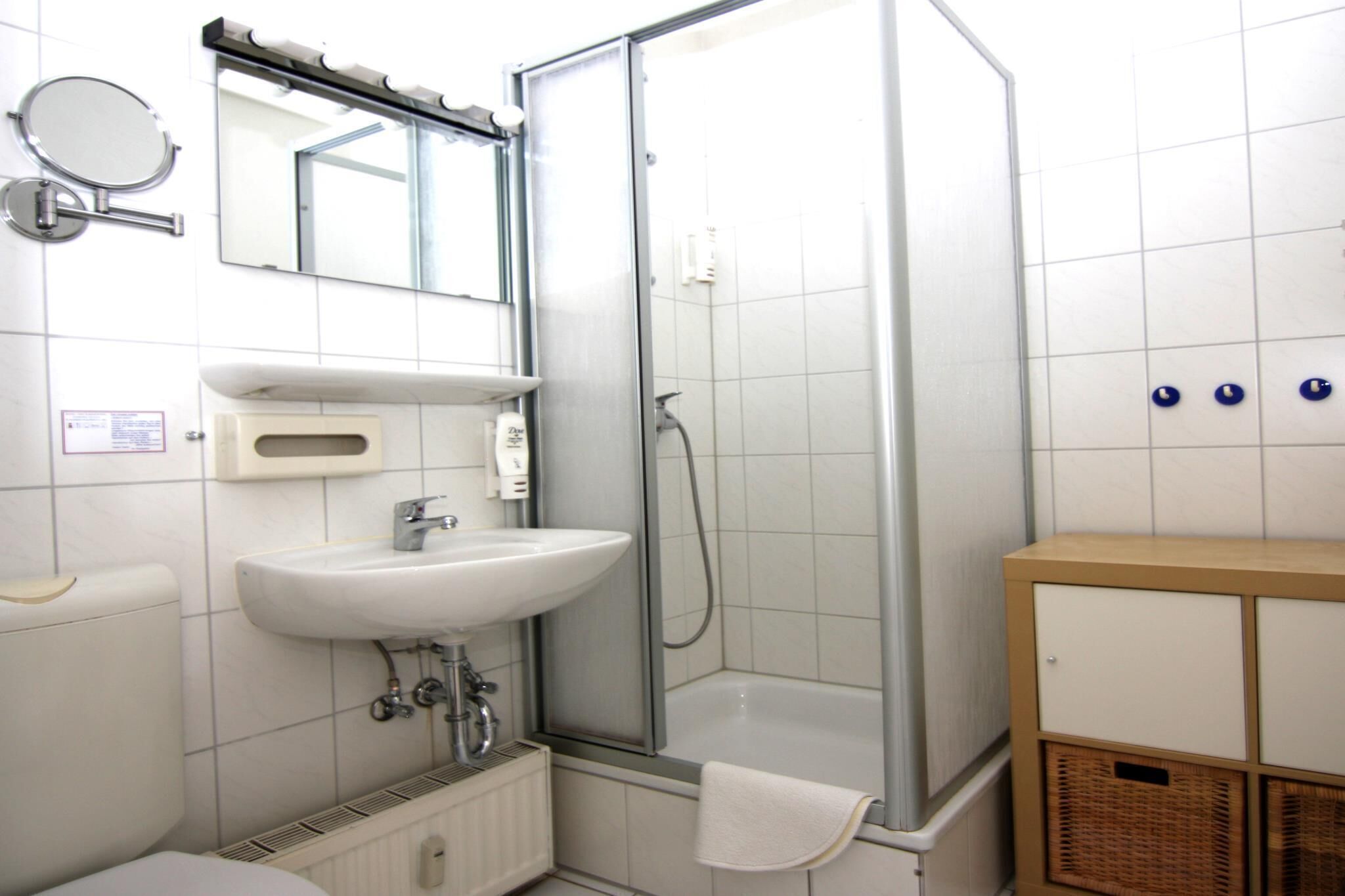 Une salle de bain avec un lavabo blanc, un miroir, une douche en verre et un meuble en bois.