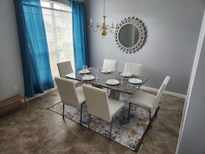 Een eetruimte met een marmeren tafel, witte stoelen en een kamerkleed met patroon.