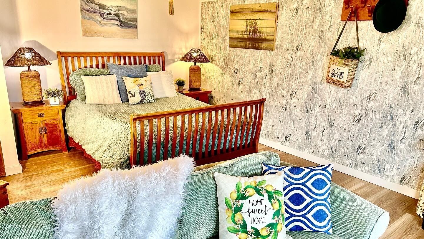 Une chambre avec un lit en bois, une table de chevet, une lampe, un mur orné d’un motif texturé et un panier suspendu.