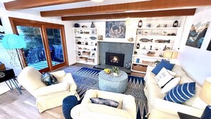 Een gezellige woonkamer met een open haard, een bijzettafeltje en een boekenplank vol decoratieve objecten.