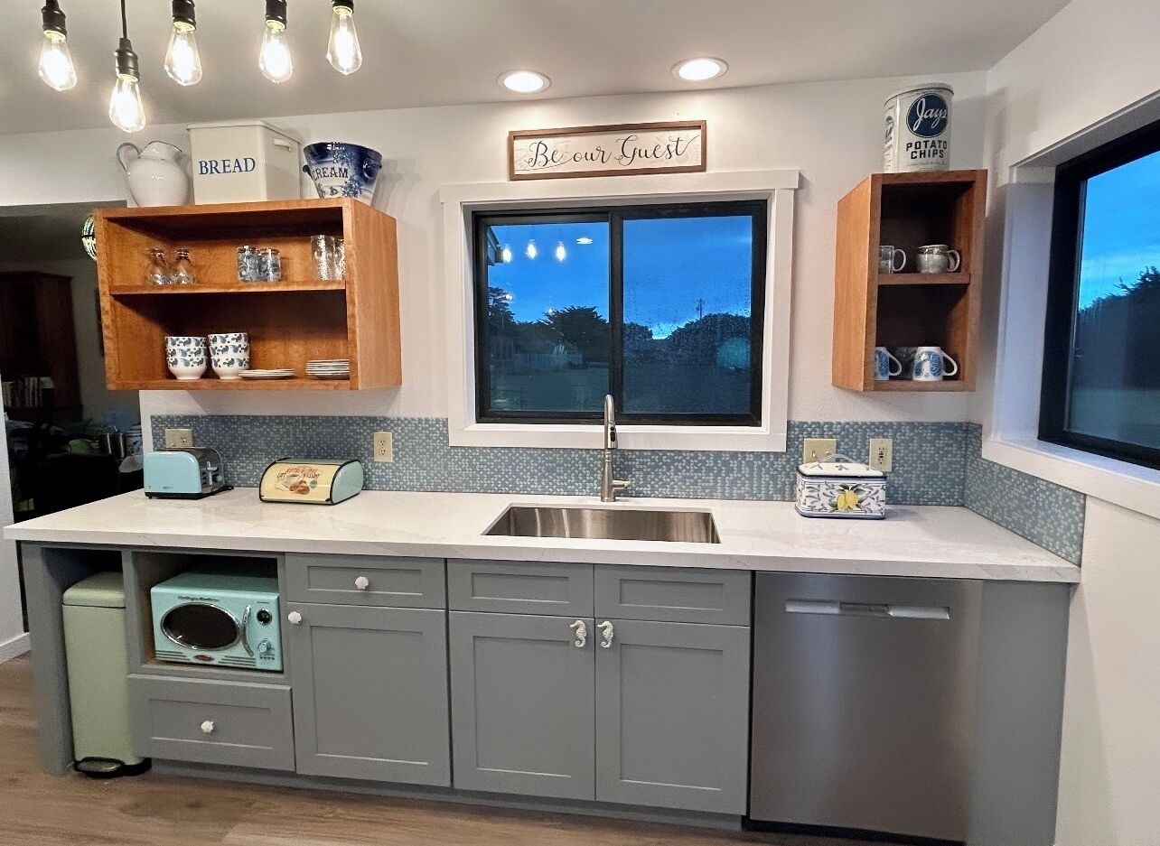 A modern kitchen with grey cabinets, a stainless steel sink, and a window with a view of the sky.