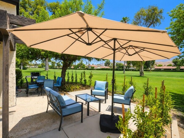 Une terrasse extérieure avec une table et des chaises, un grand parasol et une vue sur un terrain de golf.